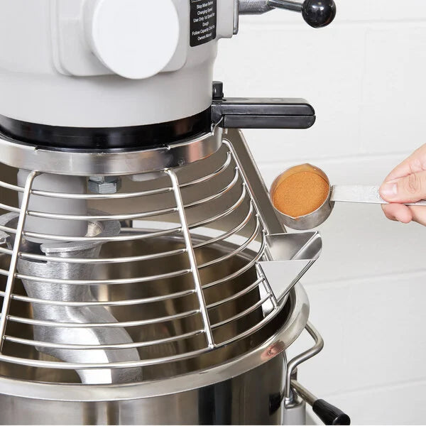 Close-up of a stand mixer with a metal bowl and a hand holding a wooden spoon.