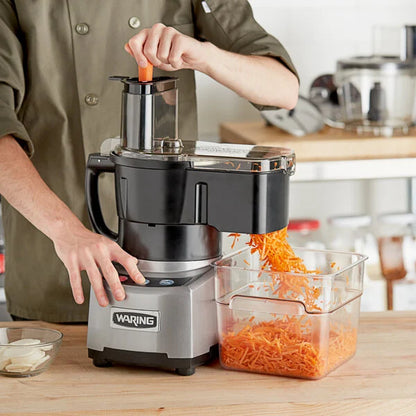 Person using a Waring food processor to shred carrots in a kitchen setting.