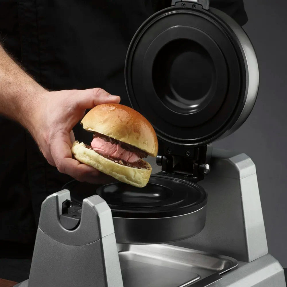 Person holding a burger above a burger press with a dark background
